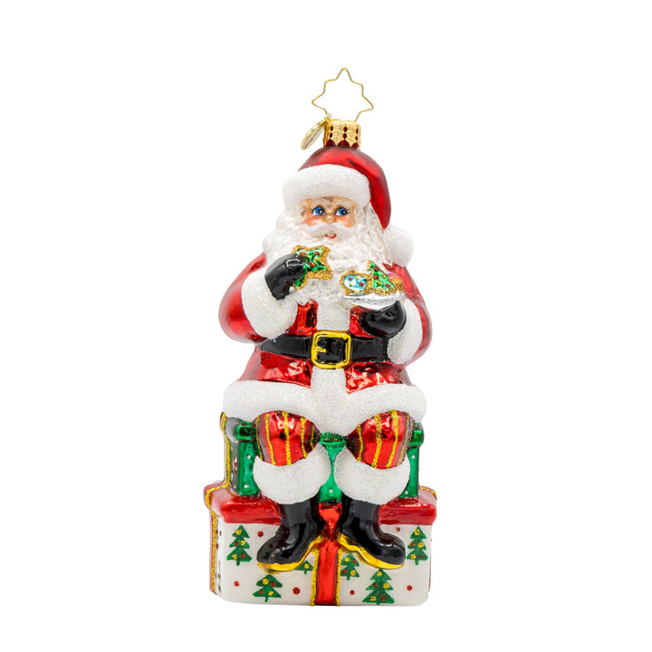 Kris Kringle's Cookie Break ornament. Santa takes a cookie break, perched atop a glittering present. View of front.