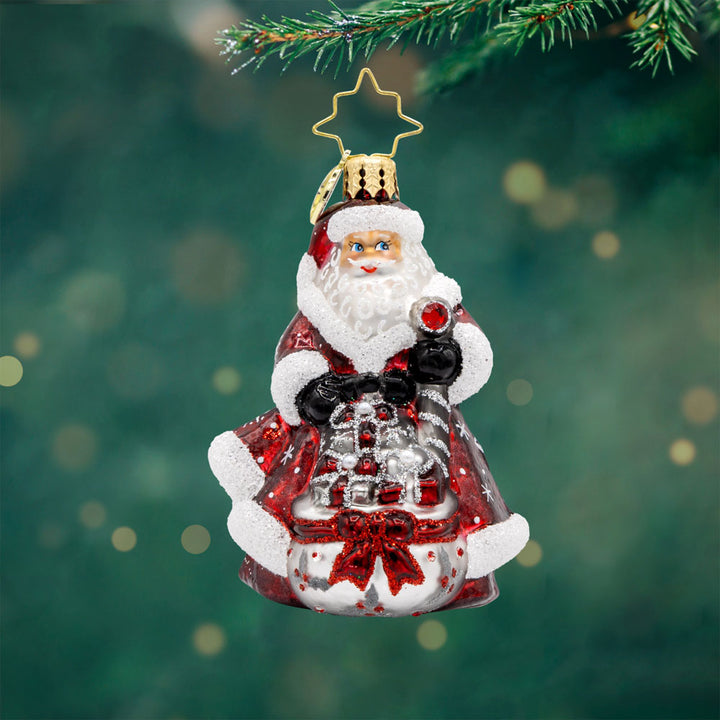 Frosty Fawn Santa Gem ornament. Santa is donned in red and silver, holding a scepter with a pile of gifts in a gift sack before him. View of front. 