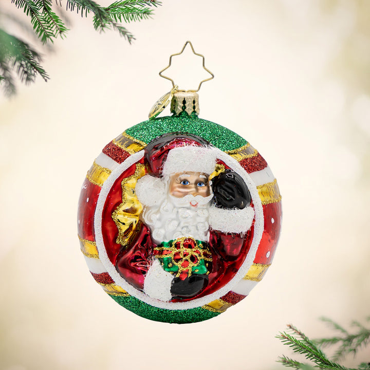 St. Nick's Spherical Cheer Gem ornament. On this ornament round of striped, red, green, and gold, Santa is seen carrying a gift. View of front. 