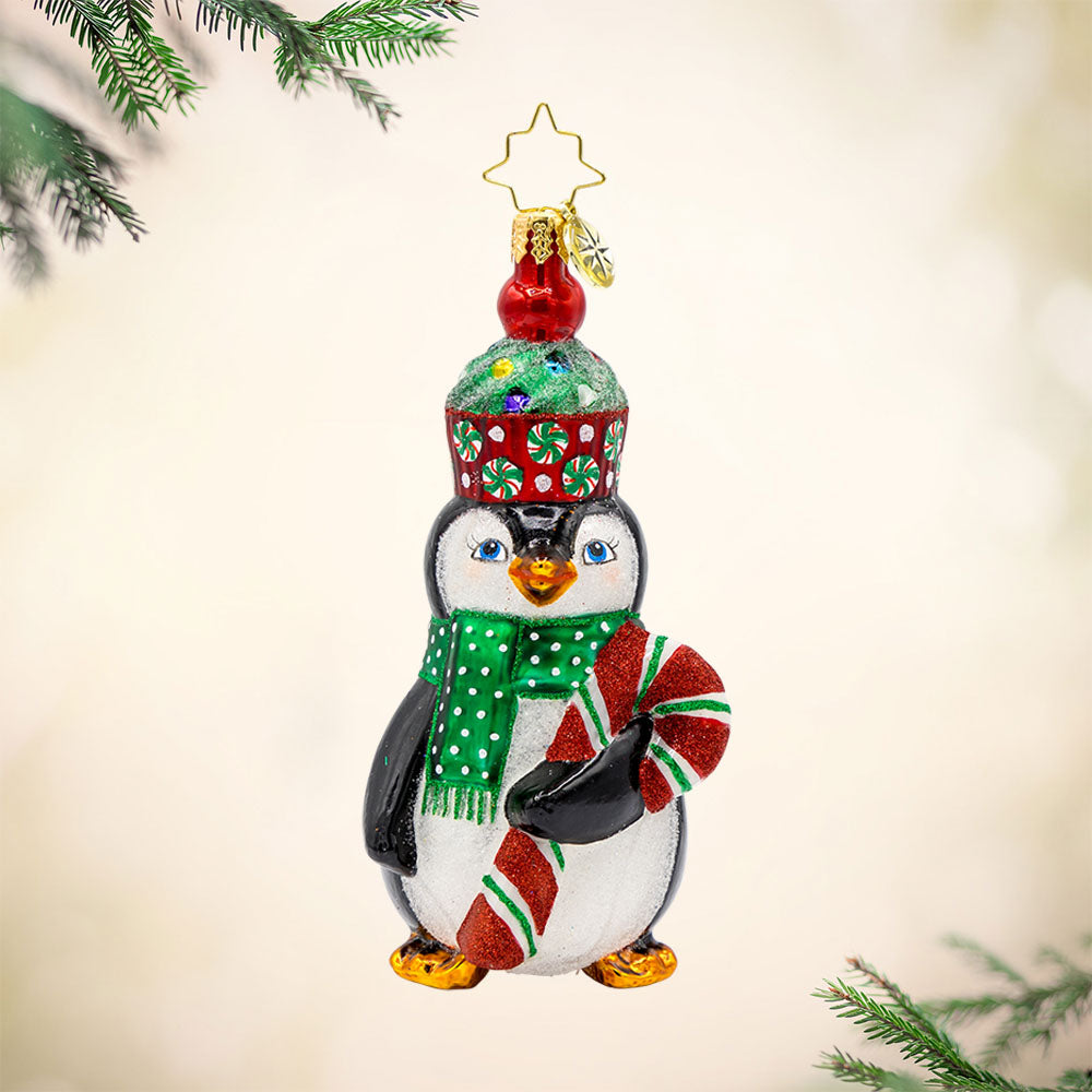 Cupcake Clad Penguin ornament. This penguin wears a cupcake hat topped with sprinkles and a festive candy cane in hand. View of front. 