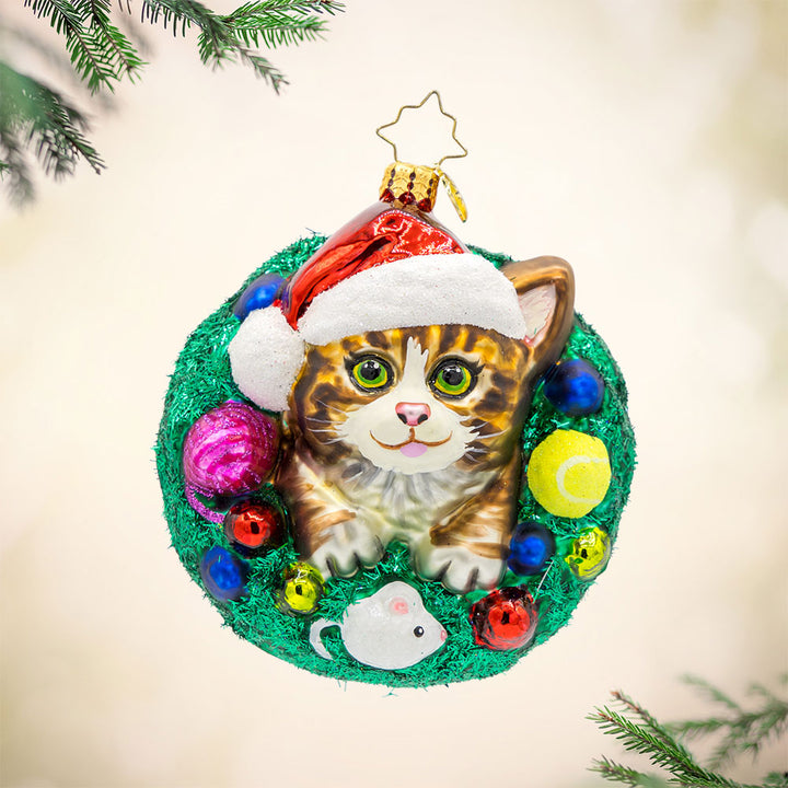 Merry Catmas ornament. Features a cat wearing a Santa hat, encircled by a wreath and toys. View of front. 
