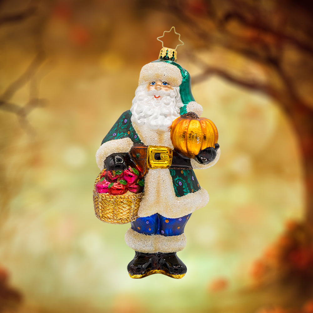Enchanted Evergreen Santa ornament. Dressed in his finest fall attire, he has a basket of apples in one hand and a pumpkin in the other. View of front. 