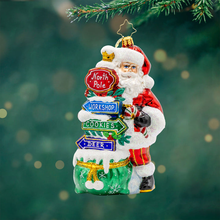 Sign of the Season Santa ornament. Santa stands next to his festive signs that will lead you to the North Pole and beyond. View of front. 