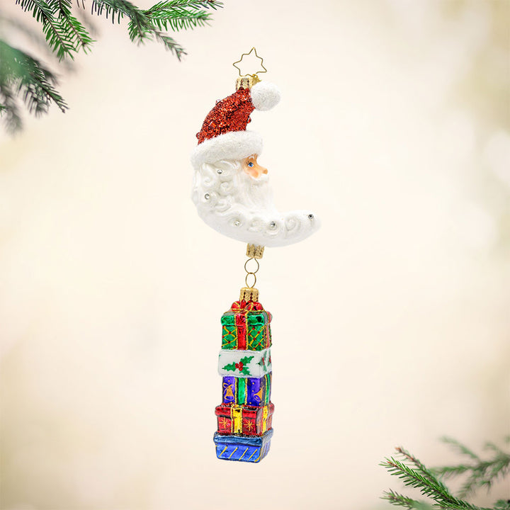 Lunar Treasures ornament. Santa's head in the shape of a crescent moon, with a stack of gifts dangling below. View of front.