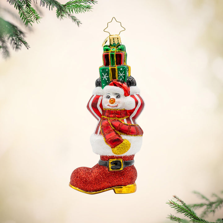 Snowman Surprise ornament. This snowman is wearing a striped sweater, popping out of a red boot, with a stack of gifts in hand. View of front. 