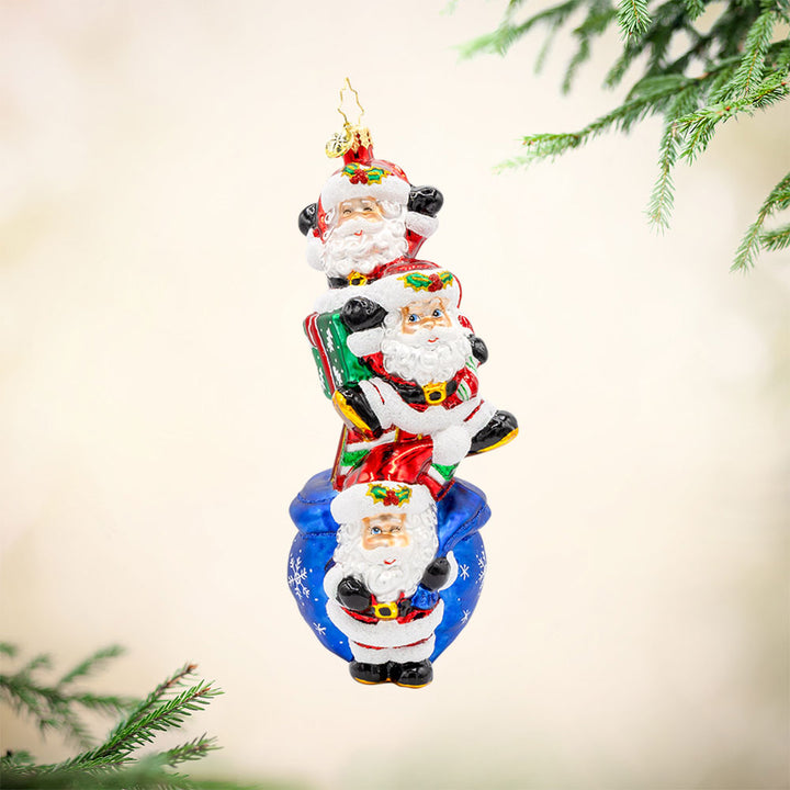 Jolly Santa Trio ornament. With their festive hats, sparkling eyes, and a bag full of gifts. View of front. 