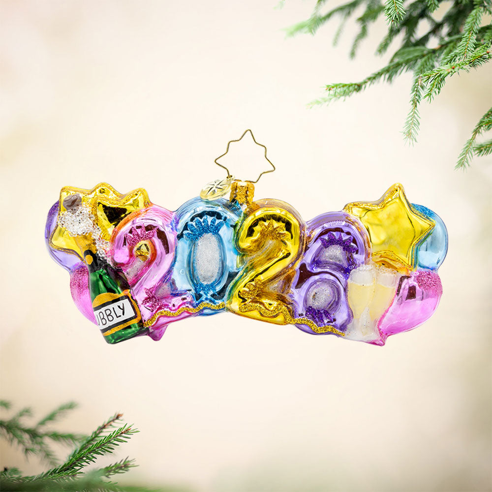 Cheers to 2026 ornament. "2026" shaped ballons in festive colors of pink, gold, blue and purple. Accompanied with a bottle of bubbles and flute glasses. View of front.