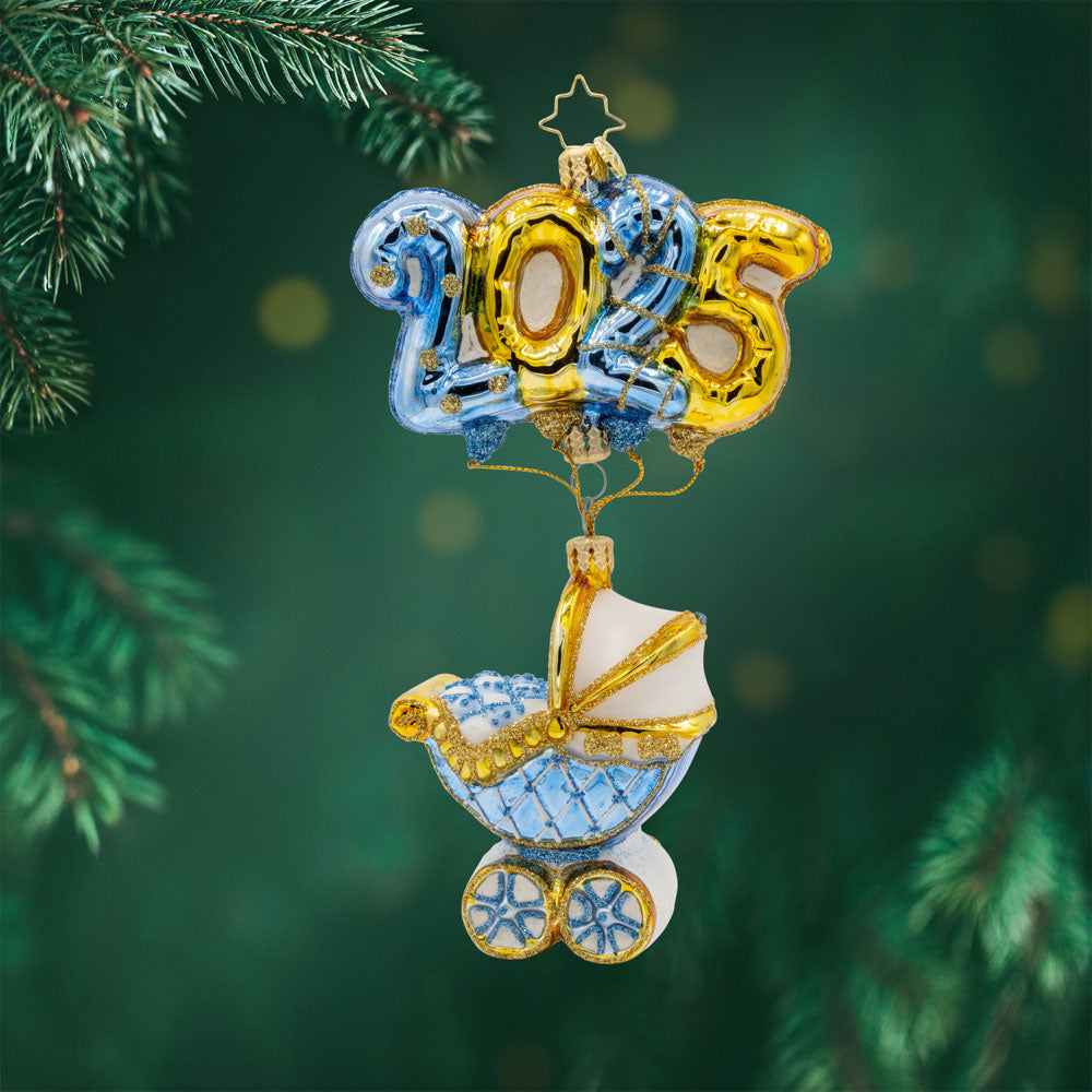 Baby Blue Cradle of Celebration ornament. Features a decorated baby blue carriage and "2025" shaped balloons. View of front. 