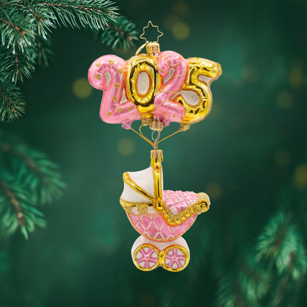 Baby Pink Cradle of Celebration ornament. Features a decorated baby pink carriage and "2025" shaped balloons. View of front. 