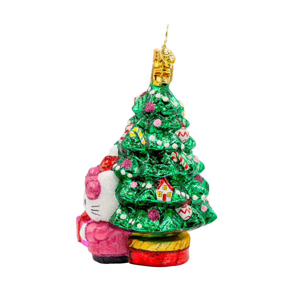 Hello Kitty's Christmas Cheer ornament. Hello Kitty is bundled up in red and pink in front of a decorated Christmas Tree. View of right side.