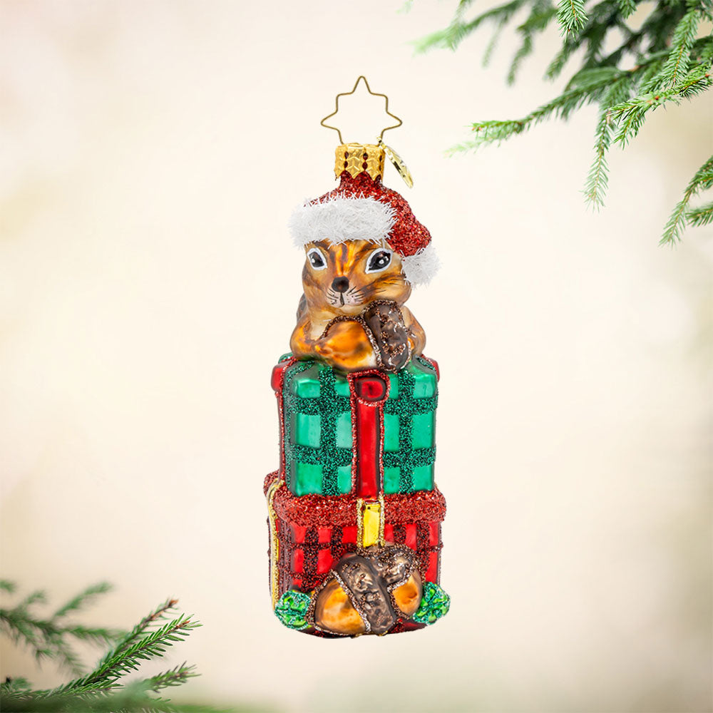 Chipper Cheer ornament. A chipmunk sits atop a stack of gifts with an acorn in hand. View of front.