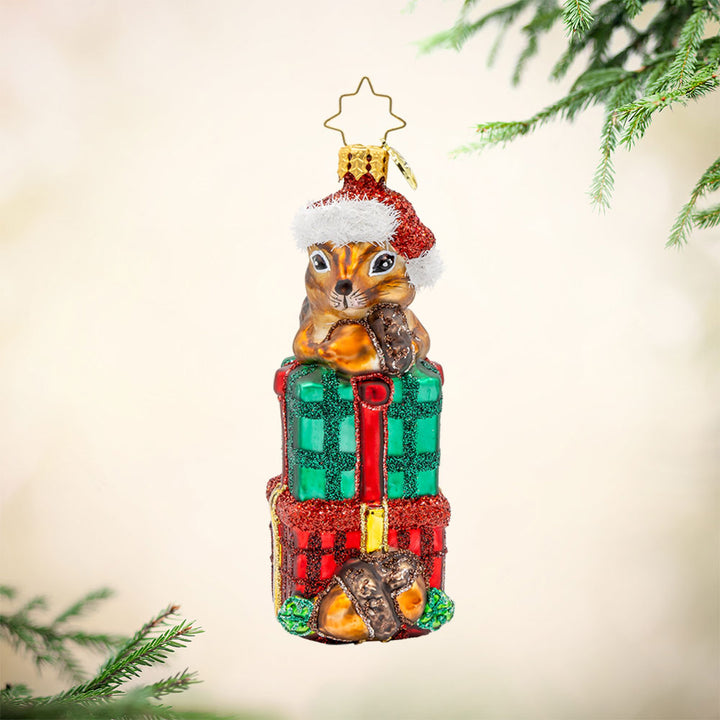 Chipper Cheer ornament. A chipmunk sits atop a stack of gifts with an acorn in hand. View of front.