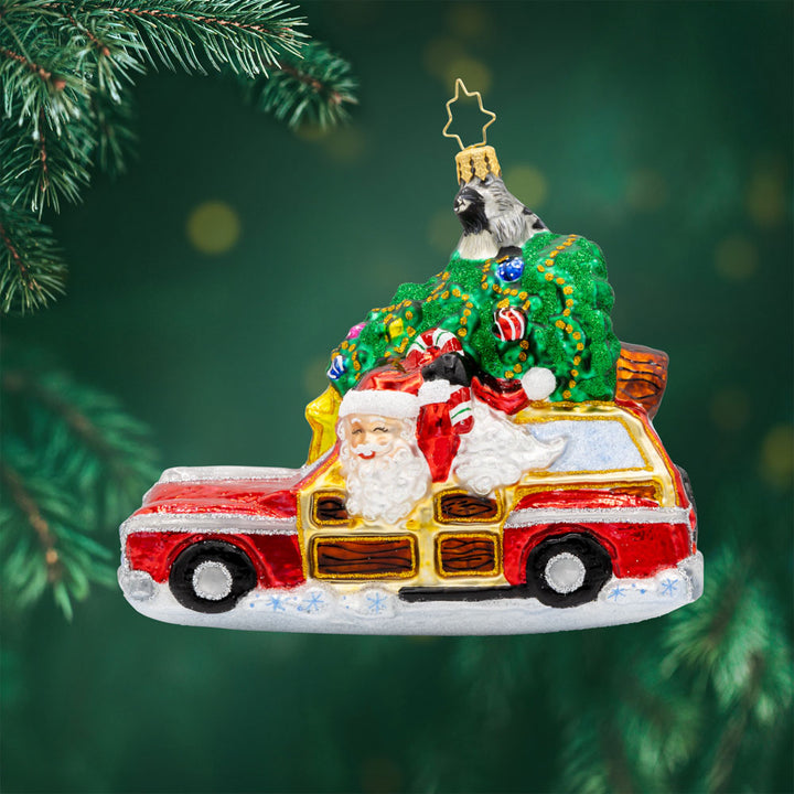 Santa's Woodland Adventure ornament. A raccoon catches a ride on the Christmas tree above Santa's car. View of front.