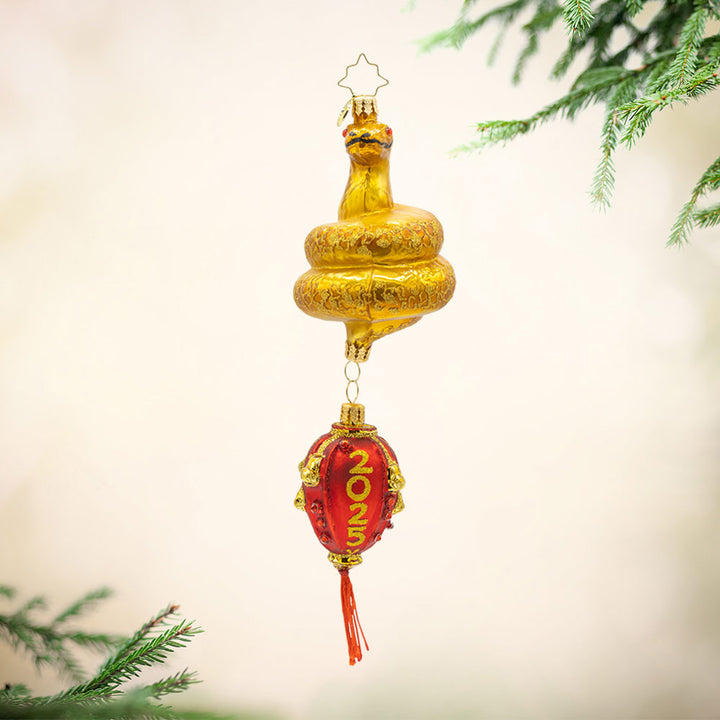 2025 Year of the Snake ornament. A red lantern dangles from a coiled gold snake, adorned with shimmering red accents View of front. 