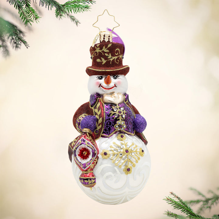 Opulent Frost. Snowman ornament in a maroon and purple suit with gold detailing's, while holding a matching-colored ornament. View of front