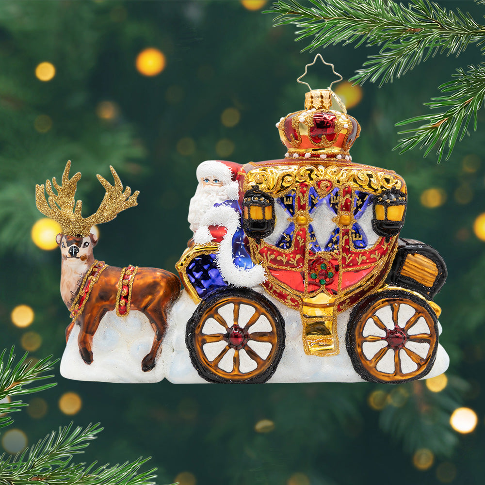 Yuletide Carriage Ride. Ornament of Santa riding in a red and gold detailed carriage while being pulled by a brown reindeer. View of front.