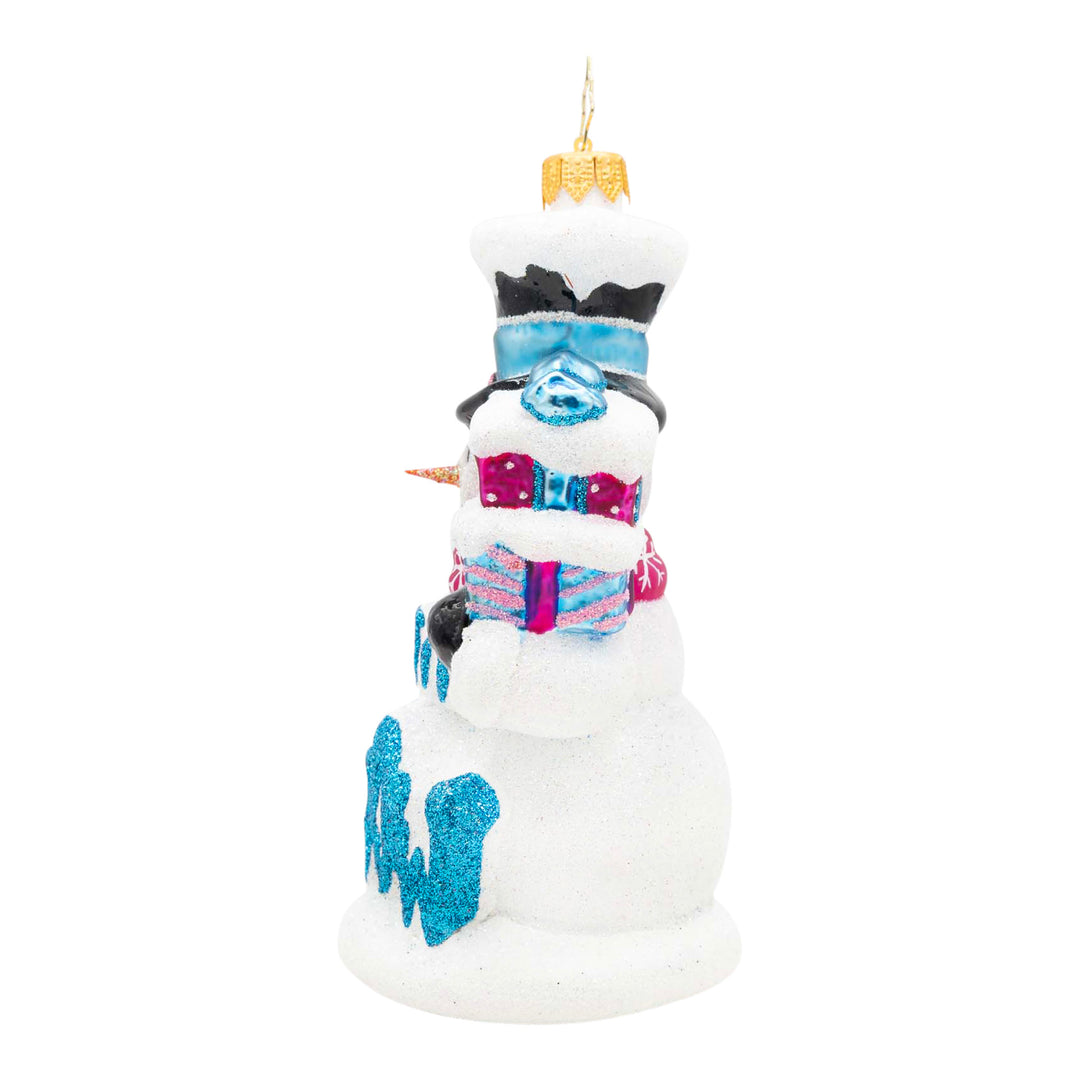 Side of a decorative snowman ornament holding two presents in the colors pink and blue in one had and in the other a broom, with the phrase "Let It Snow" in blue on the front. 