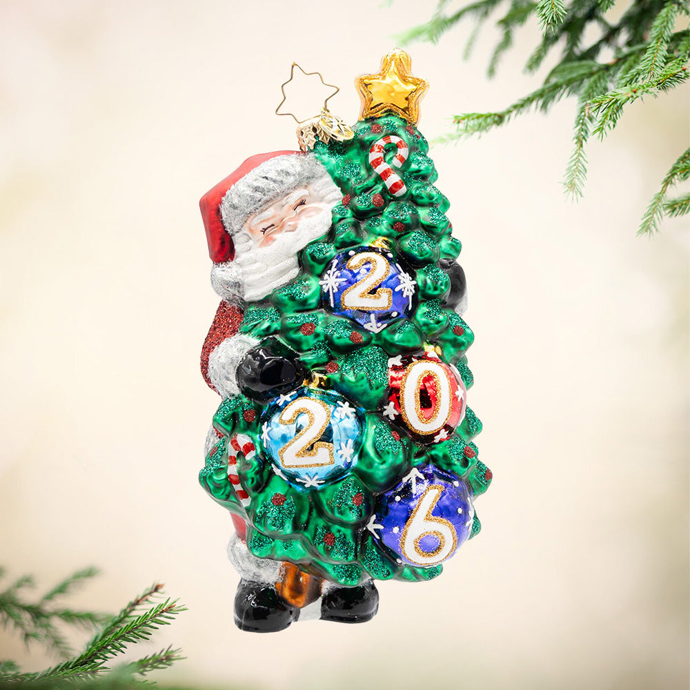 Decked for 2026. Santa holding a decorated tree with the year 2026 painted on the ornament. View of front