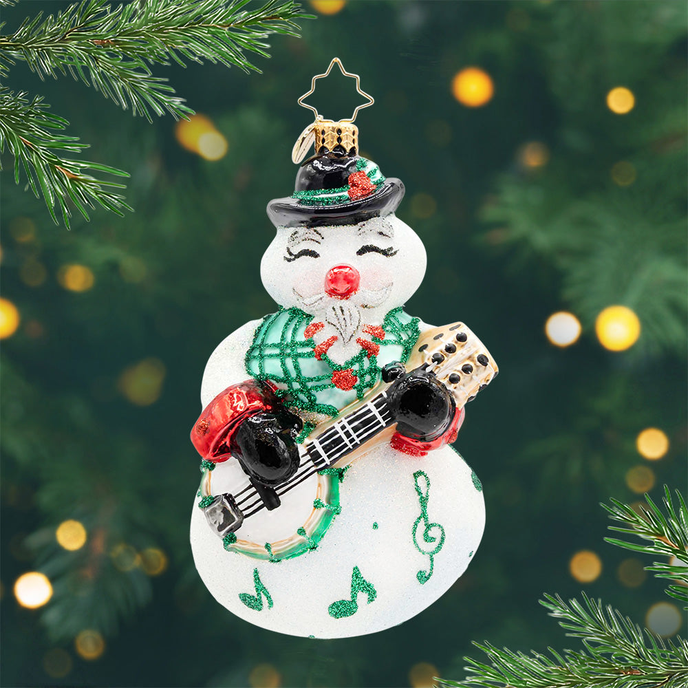 North Pole Notes. Snowman ornament wearing a green scarf with details of music notes and playing a green and brown banjo. View of front