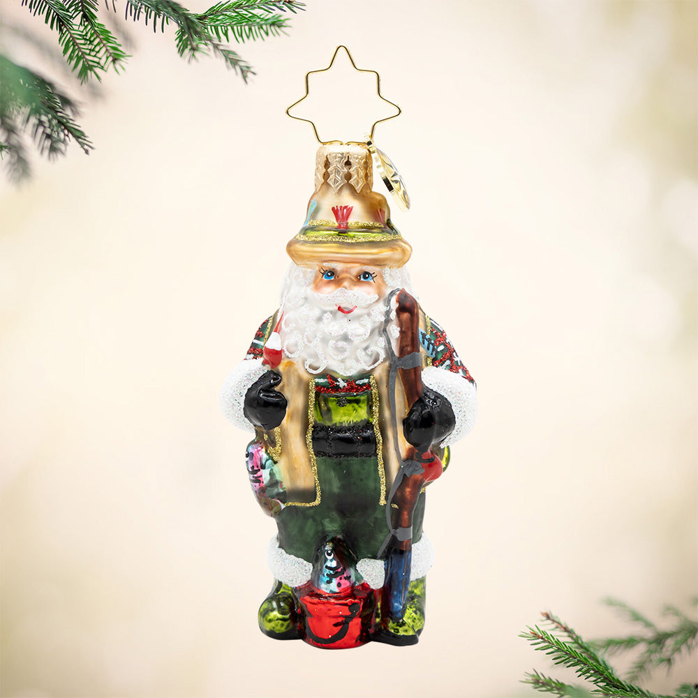 Fly Fisher Claus Gem. Ornament of Santa dressed in a green and brown fishing outfit with a red bucket and brown fishing pole. View of front