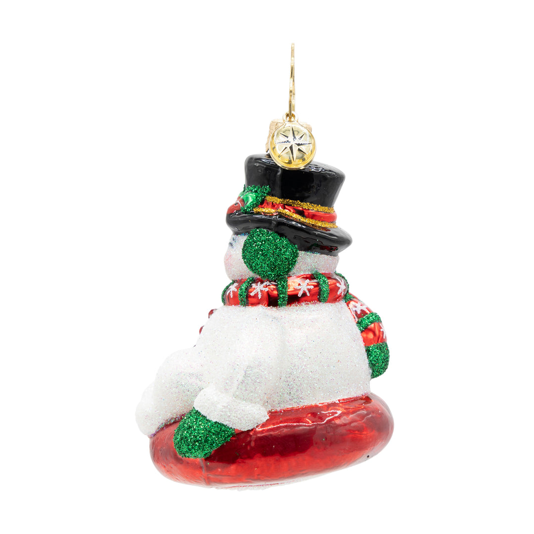 Side view of ornament of a snowman wearing a red and green scarf on a red sled. 