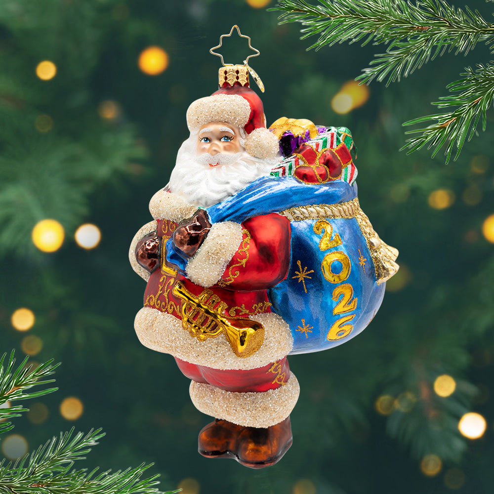 2026 A Bag Full of Memories. Santa in his signature red suit, carrying a blue bag of presents with a label for 2026. View of front.