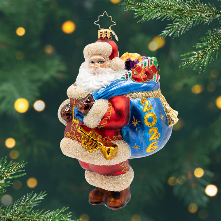 2026 A Bag Full of Memories. Santa in his signature red suit, carrying a blue bag of presents with a label for 2026. View of front.