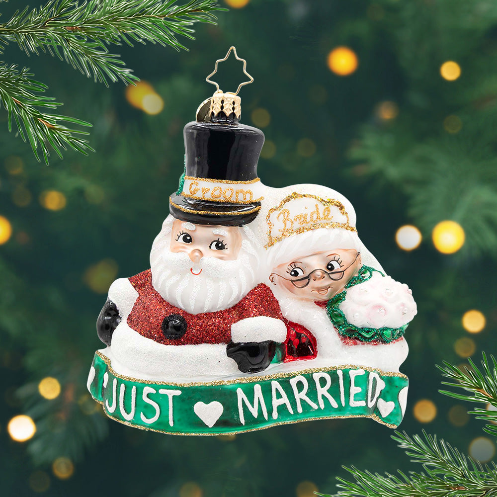 Merry Matrimony. Ornament of Mr. and Mrs. Clause with groom and bride on their hats and a green banner with the phrase "I just married beneath them. View of front
