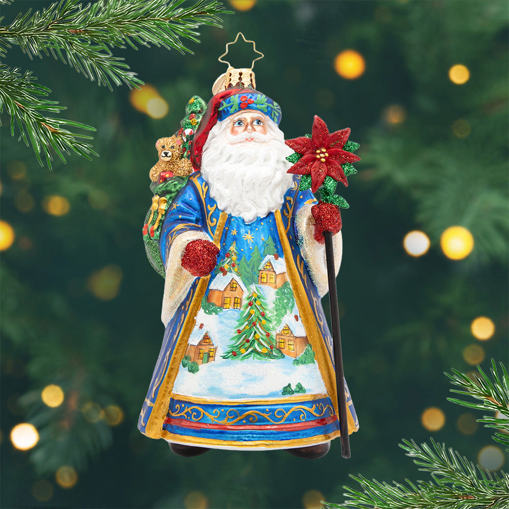 Father Christmas’ Eve. Ornament of Santa dressed in regal blue with a golden staff and starry cloak and a peaceful winter village scene on his robe. View of front