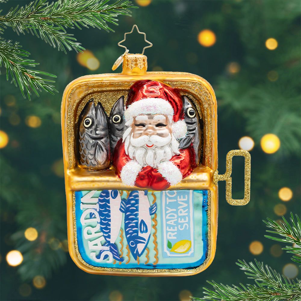 Holiday in a Tin. Ornament of Santa in a gold and blue sardine can with three other grey sardines. View of front