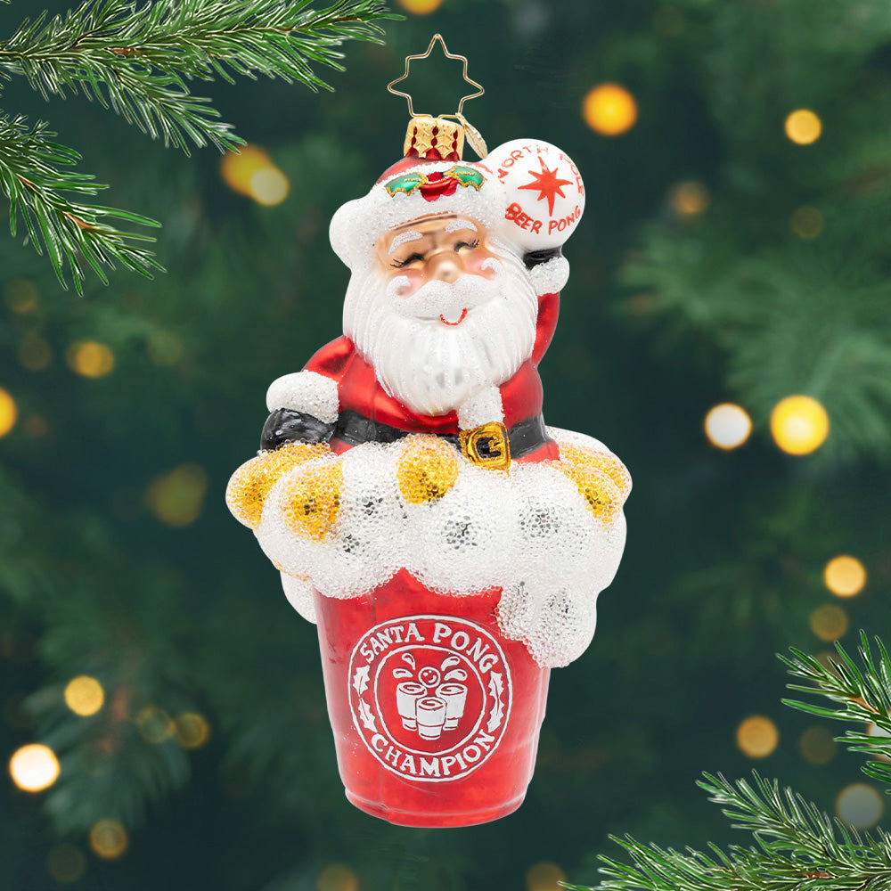 Santa Pong Champion. Santa ornament of him popping out of a sparkly red and frothy cup while holding a ping pong ball with the phrase "North Pole Beer Pong' and "Santa Pong Champion" on the front of the cup. View of front