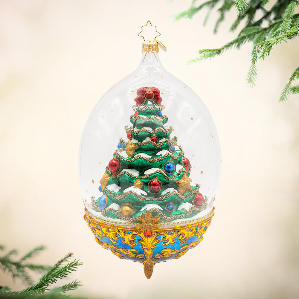 Royal Elegance Spruce. Ornament of a bright green spruce tree decked in gold ribbon and gems of gold, red, and blue, while inside a dome with a blue and gold base.