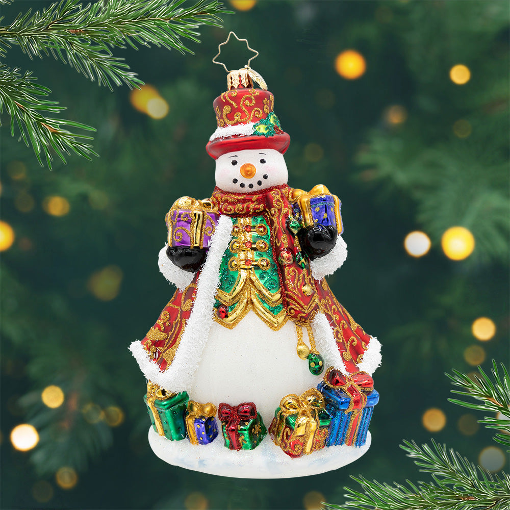 The Jingle Gent. A snowman ornament dressed in a red and gold robe  with a matching top hat, surrounded by and holding presents. View of front.