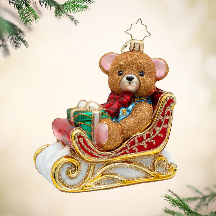 Beary Merry Sleigh. A red and gold ornament of a sleigh holding a sparkly brown bear and a green present. View of front.