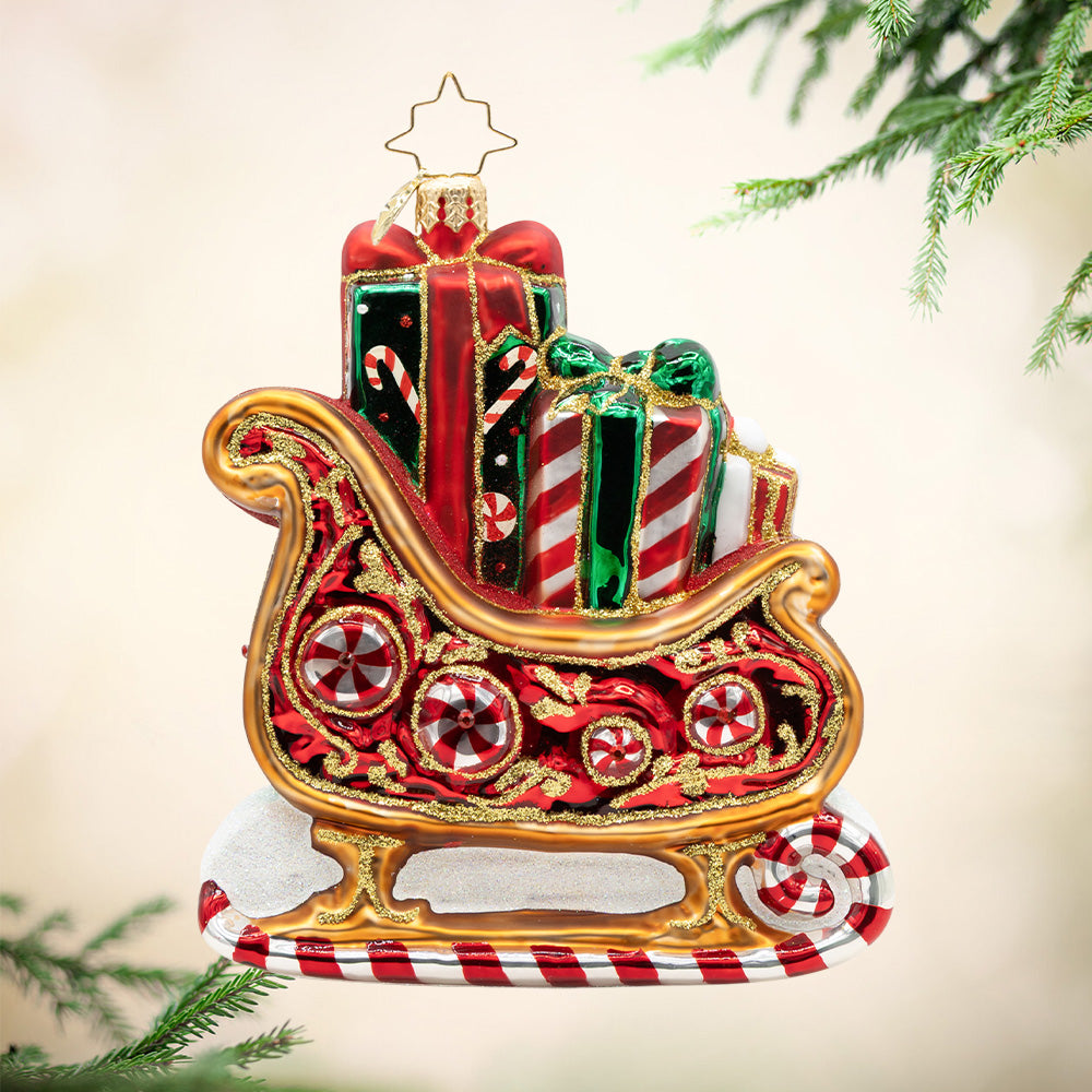 Sweetest Sleigh Ride. A red and gold ornament of Santa's sleigh carrying presents with different red and green patterns. View of front