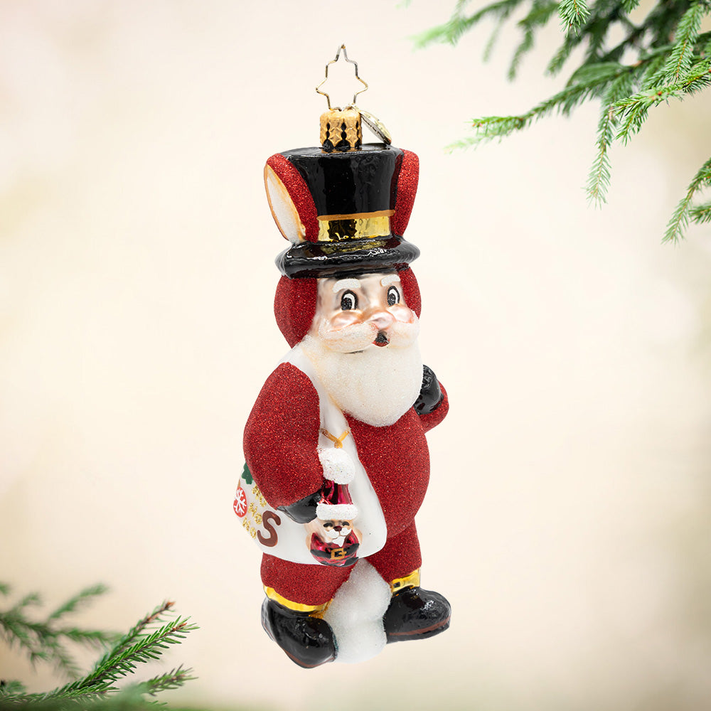 A Santa for Santa. An ornament of Santa wearing a red sparkly bunny suit and carrying a white bag and a mini him. View of front