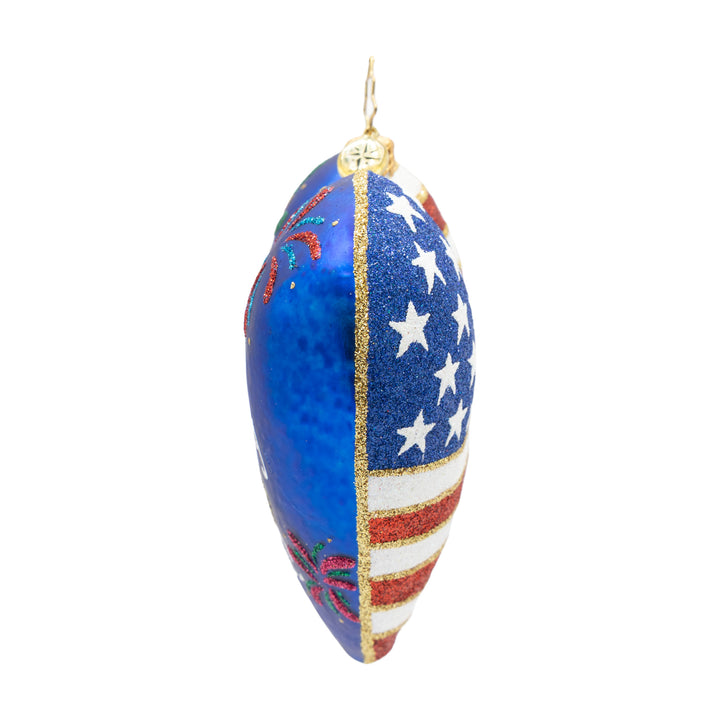 Side view of a heart shaped ornament with gold, red and white on the right side and blue, gold and green on the left side. White background.