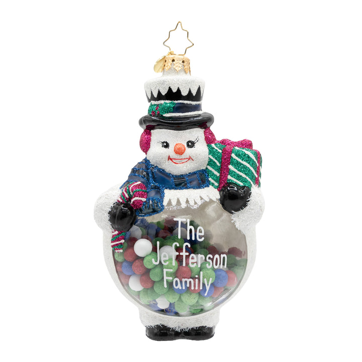 A personalized snowman ornament with a clear glass body filled with colorful candies, featuring a glittery blue scarf, black top hat, and a green and white striped gift bag. The ornament is personalized with the text 'The Jefferson Family' and topped with a gold star.
