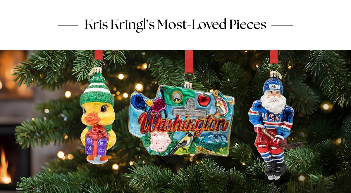 Banner titled "Kris Kringl's Most-Loved Pieces" displaying three glass Christmas ornaments hanging on a tree: a duck in a winter hat holding a gift, a Washington state landmark ornament, and a USA hockey Santa Claus.