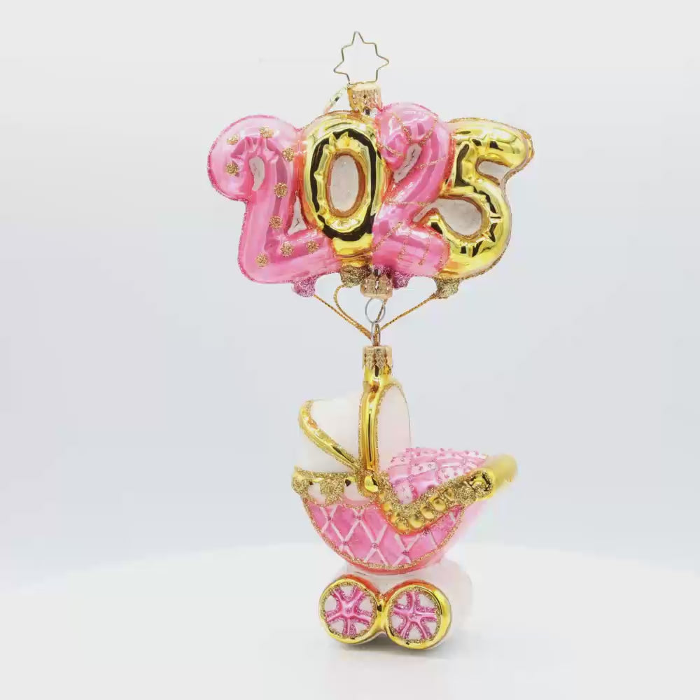 Baby Pink Cradle of Celebration ornament. Features a decorated baby pink carriage and "2025" shaped balloons. Video.